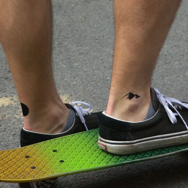 Tatouages temporaires cercle et montagnes noirs de la planche "daily minimal" appliqués sur la cheville d'un homme