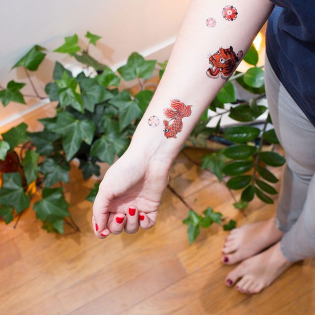 tatouages temporaires tigre, poisson et fleur de la planche "tigerwood" appliqués sur le bras d'une femme.